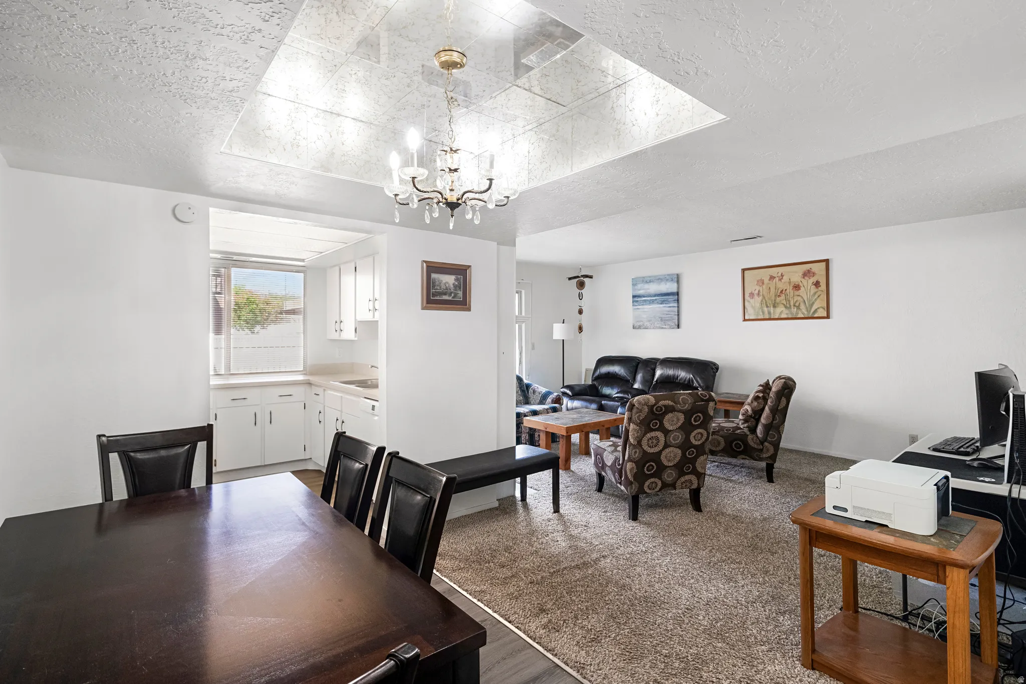 Open-concept living space with a dining area featuring a chandelier and recessed ceiling detail