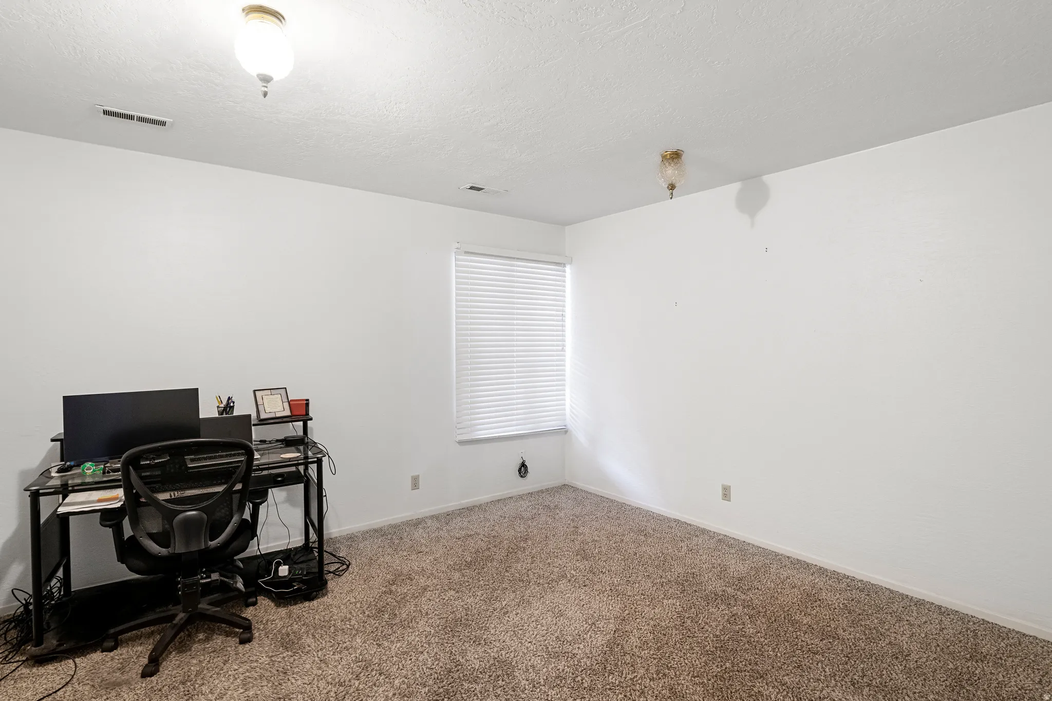 Room with textured white walls, a single window with horizontal blinds, and neutral-toned carpet flooring