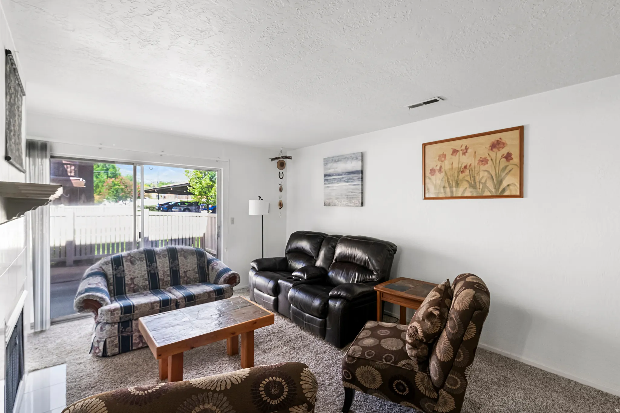 Living area with sliding glass door access to a private patio, featuring neutral wall paint, textured carpeting, and a built-in fireplace