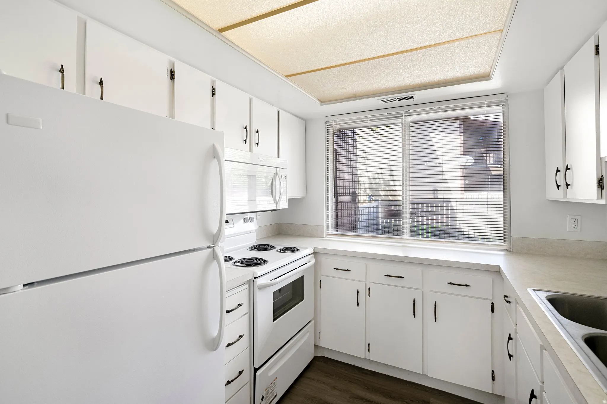 White kitchen cabinetry with black hardware, white appliances, and a window with blinds