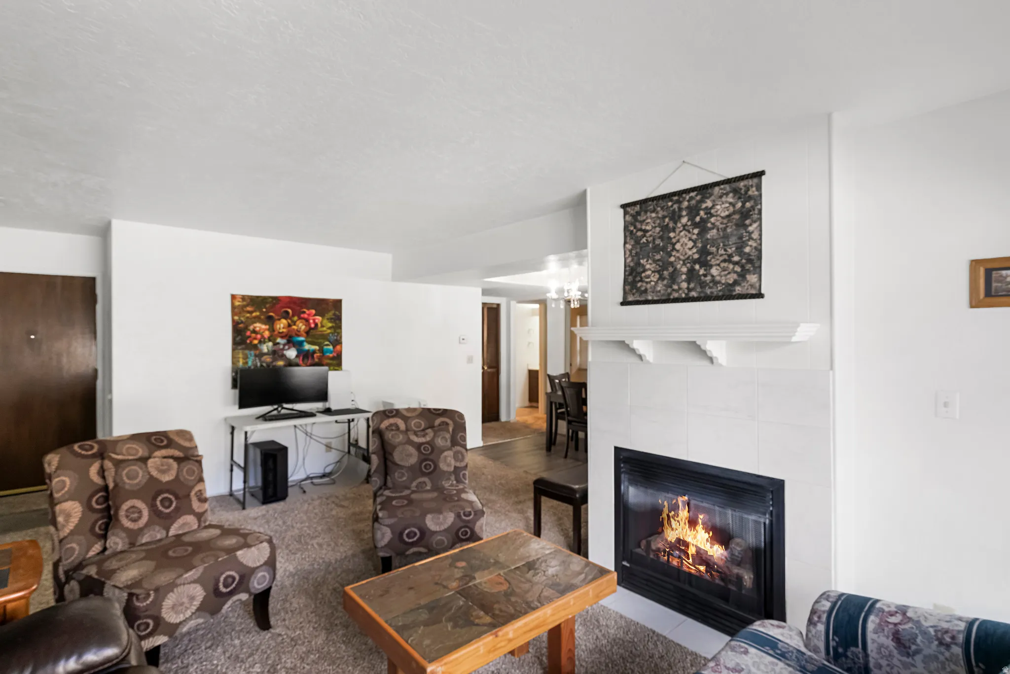 Living area featuring a tiled fireplace with mantel, textured carpeting, and white walls