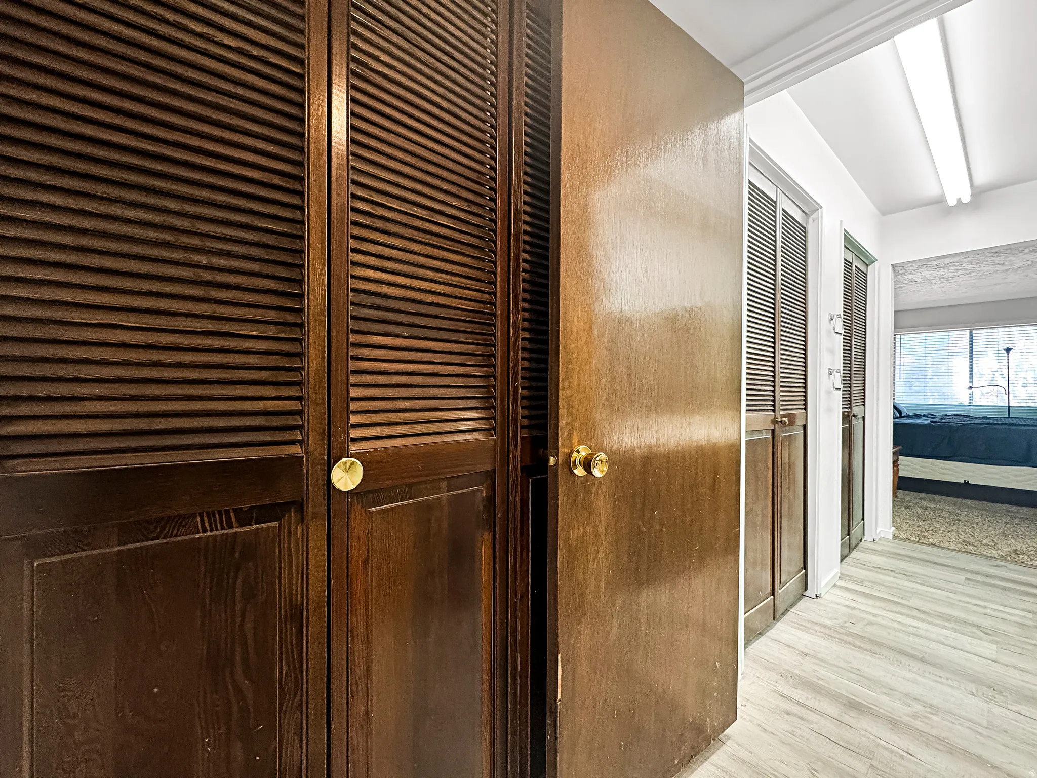 Hallway featuring dark wood bi-fold louvered doors, a light wood-finish flooring, and white painted walls
