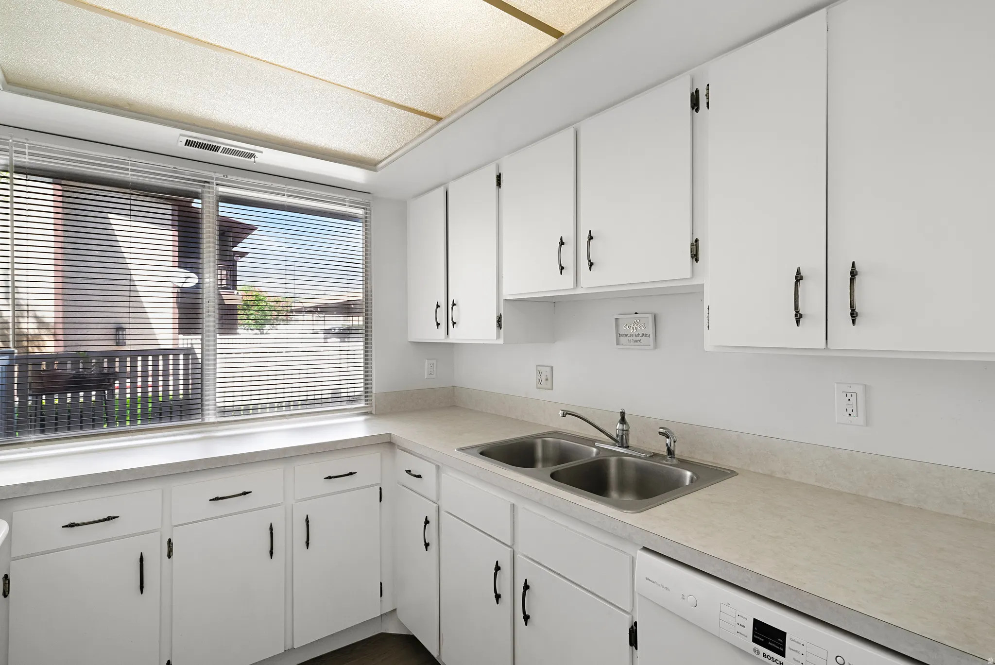 Kitchen featuring white cabinetry with dark hardware, a dual-basin stainless steel sink, and light-toned countertops