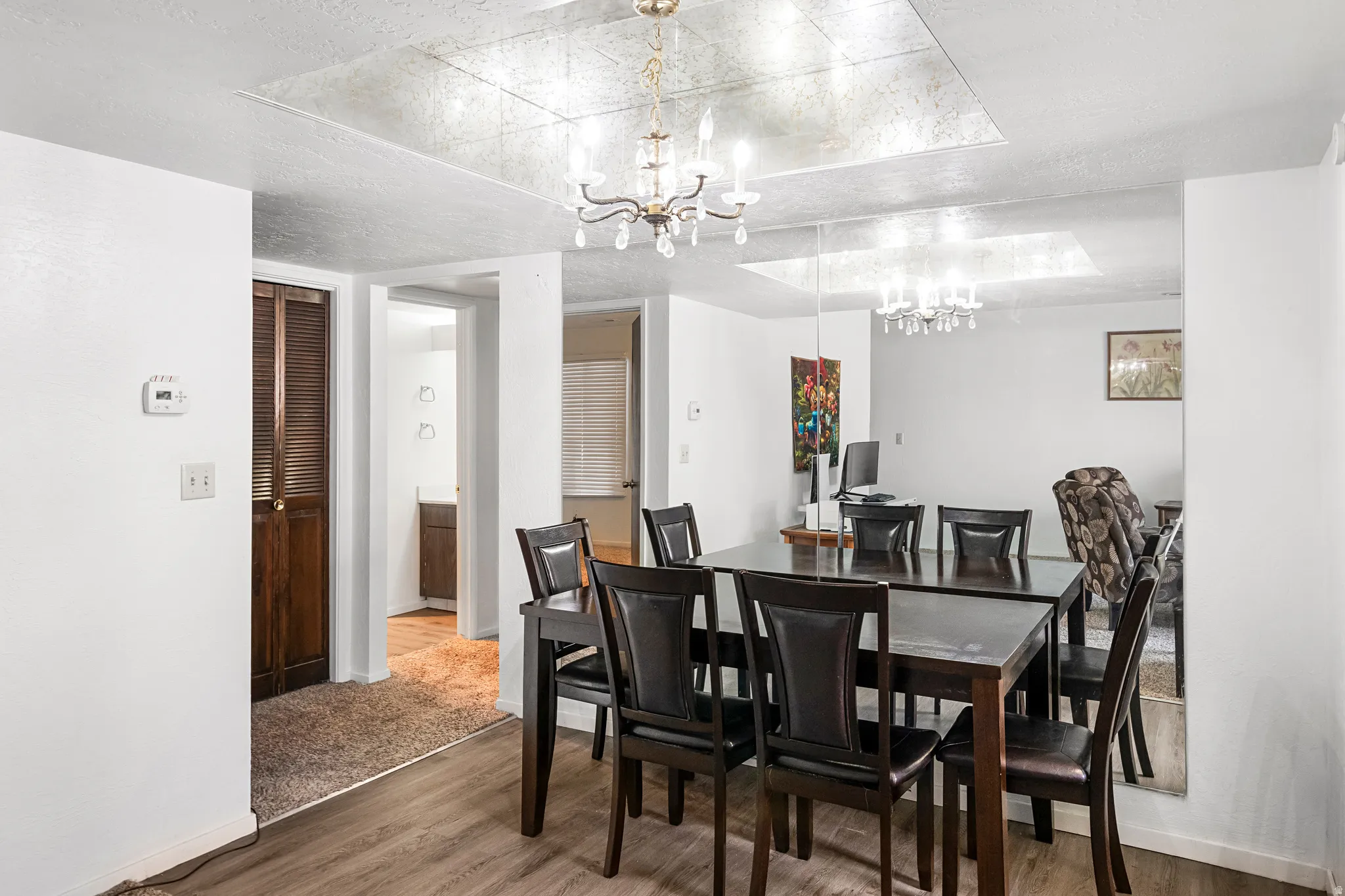 Dining area featuring wood-finish flooring, a chandelier with crystal accents, and a mirrored wall panel