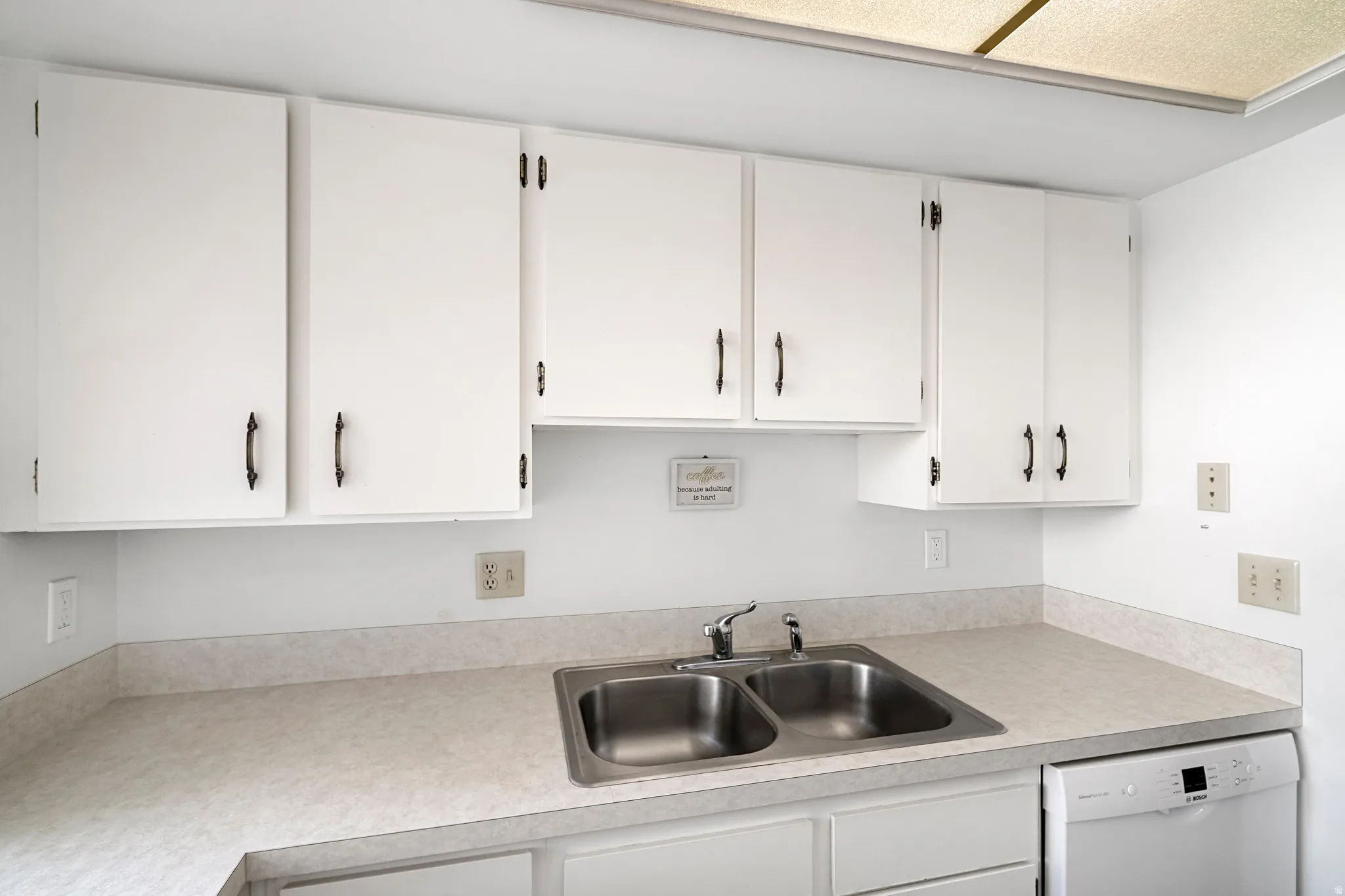Kitchen featuring white cabinetry with dark hardware, a double basin stainless steel sink, and light-toned countertops