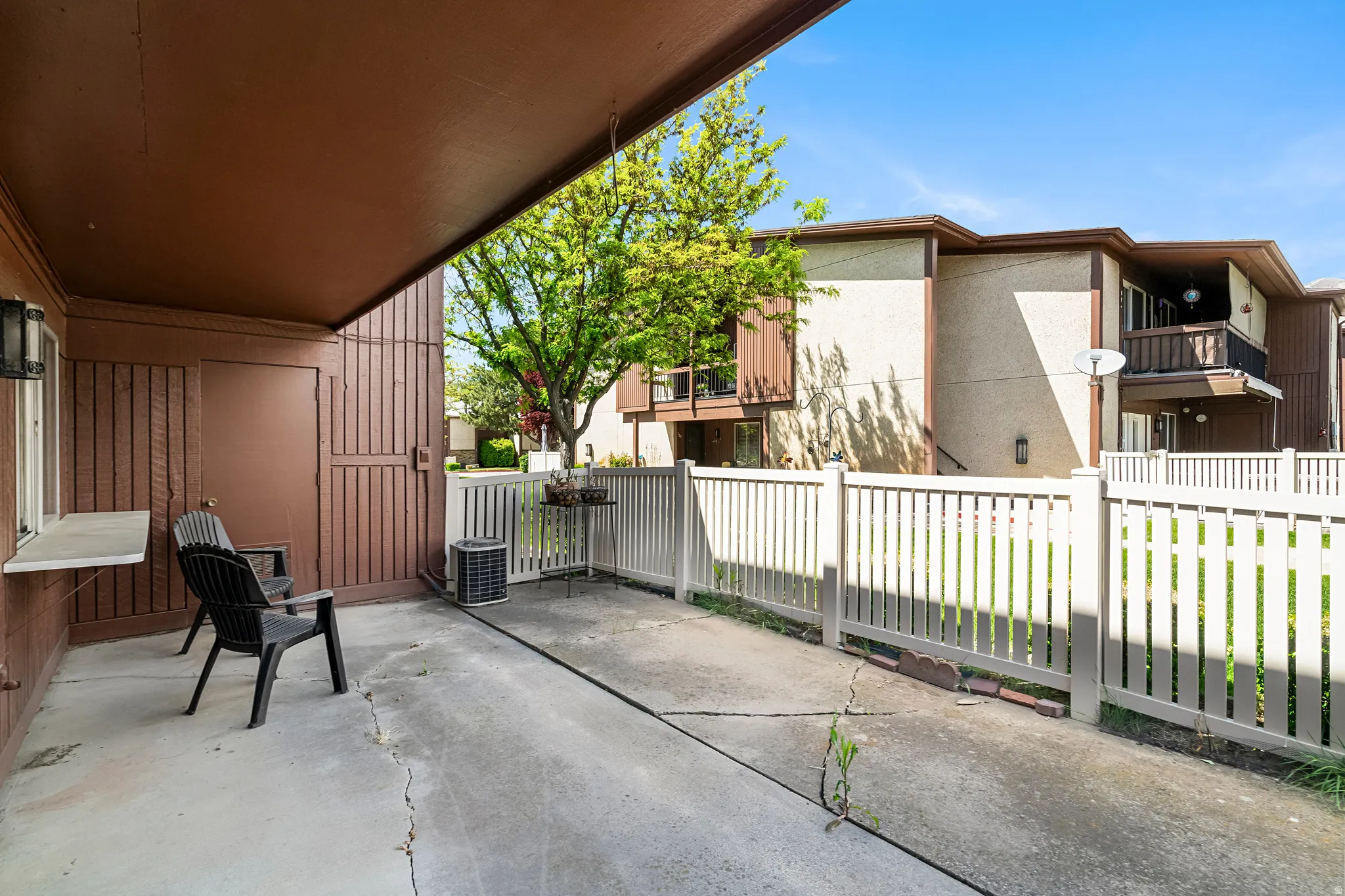 Covered patio featuring a concrete surface, brown vertical siding, a window ledge, and a white picket fence