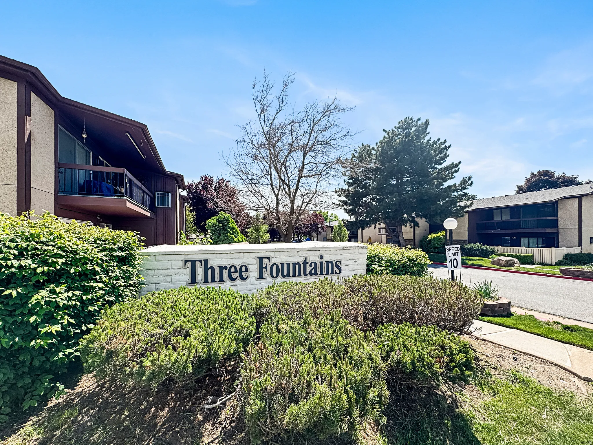 Community entry sign with raised lettering, surrounded by established shrubs and mature trees