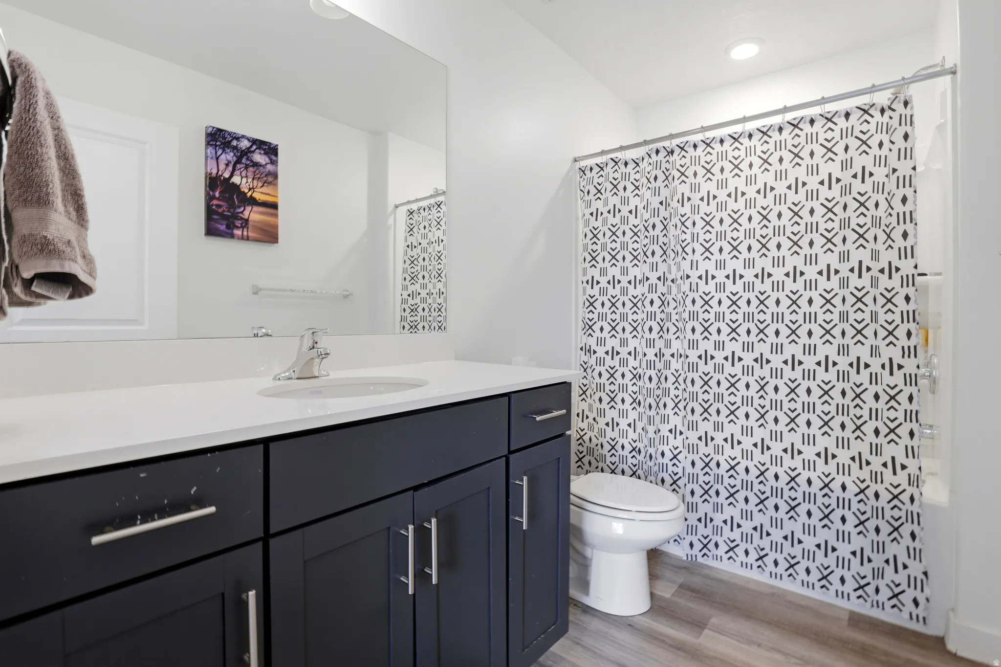 Bathroom featuring a dark wood-finish vanity with a white countertop, an integrated sink with chrome faucet, a white toilet, and a white tub with shower