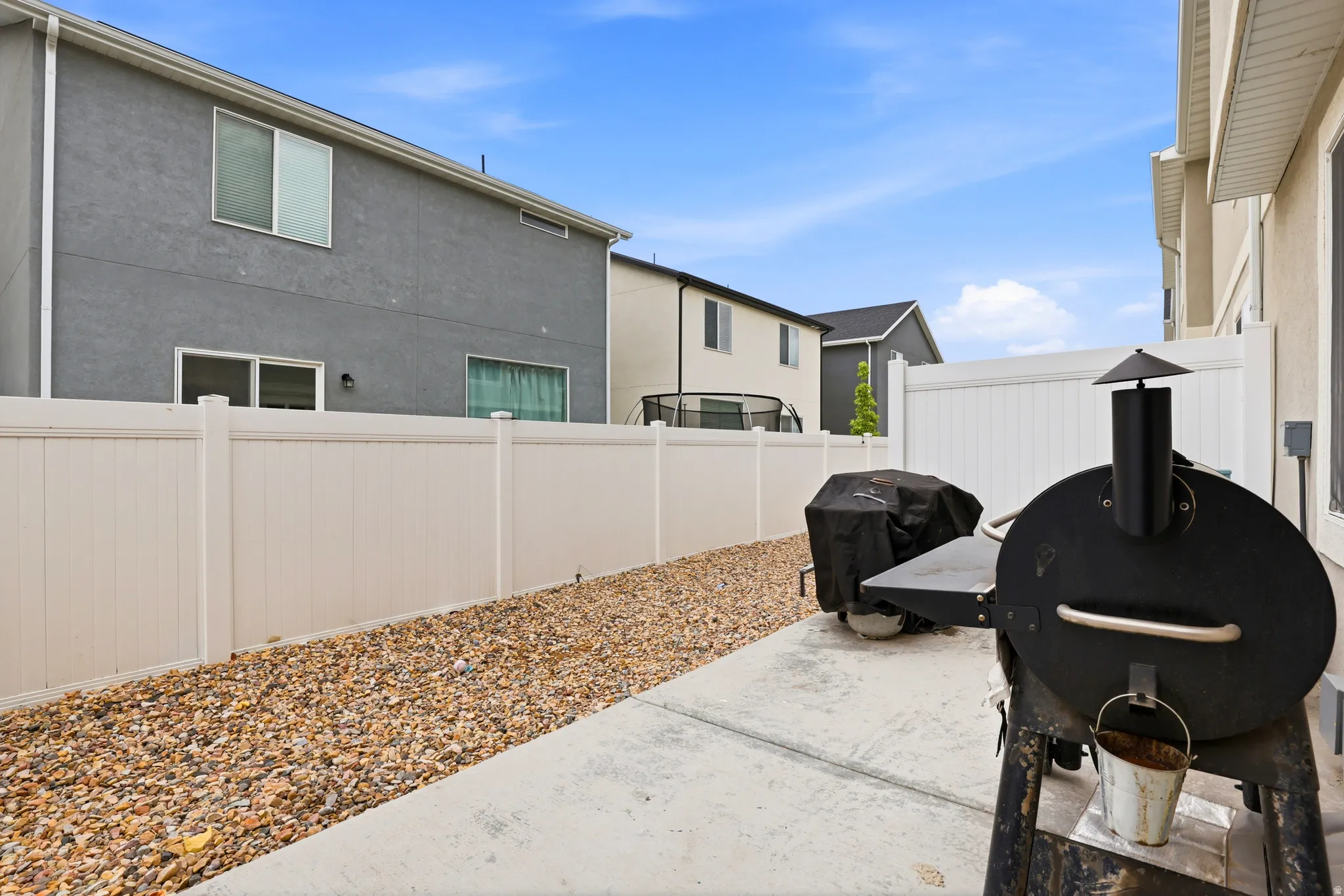 Outdoor patio area featuring a concrete slab, gravel landscaping, and a white privacy fence