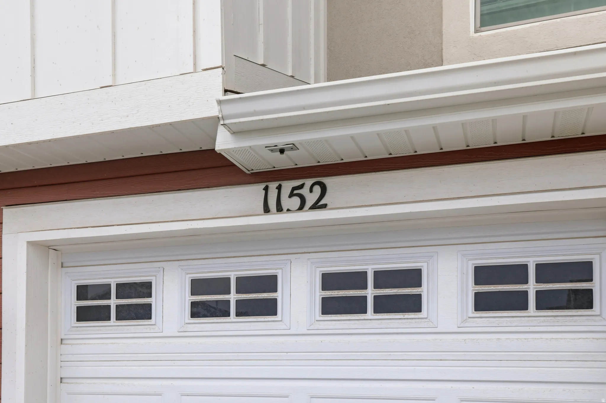 White paneled garage door with upper window inserts, featuring dark house numbers prominently displayed above the garage entrance