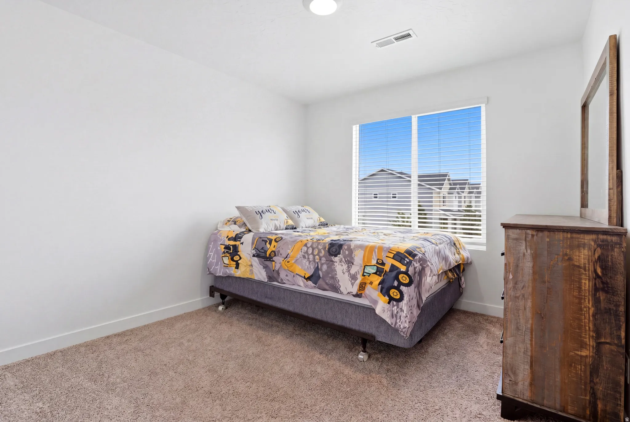 Bright bedroom featuring a large window with horizontal blinds, neutral carpeting, white walls, and a ceiling light fixture