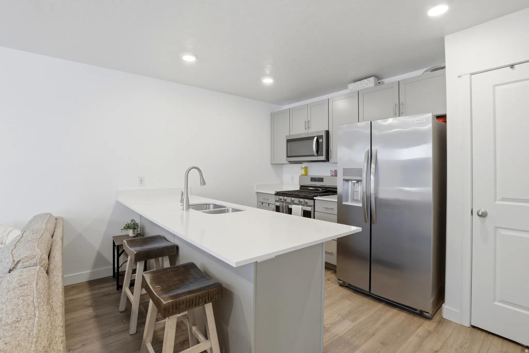 Modern kitchen featuring a breakfast bar with seating, stainless steel appliances, light gray cabinetry, and recessed lighting