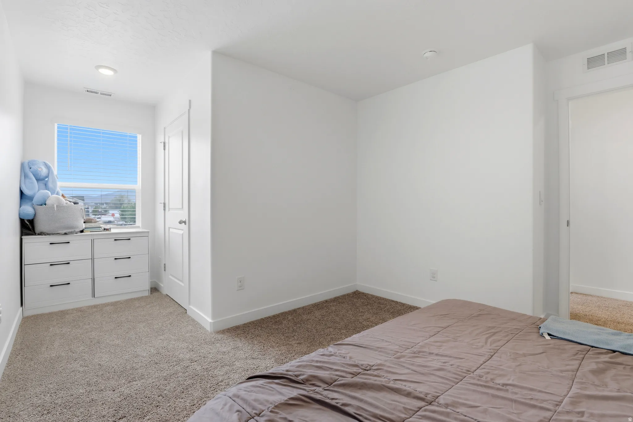 Carpeted room with a window featuring horizontal blinds, recessed lighting, and a white interior door