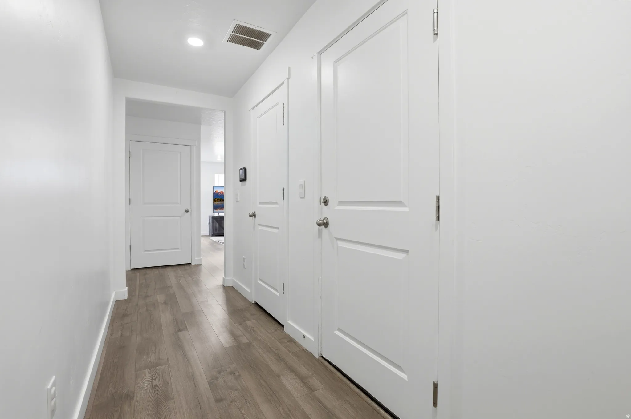 Hallway with wood-finish flooring, white walls, white baseboards, and white two-panel doors with brushed nickel hardware
