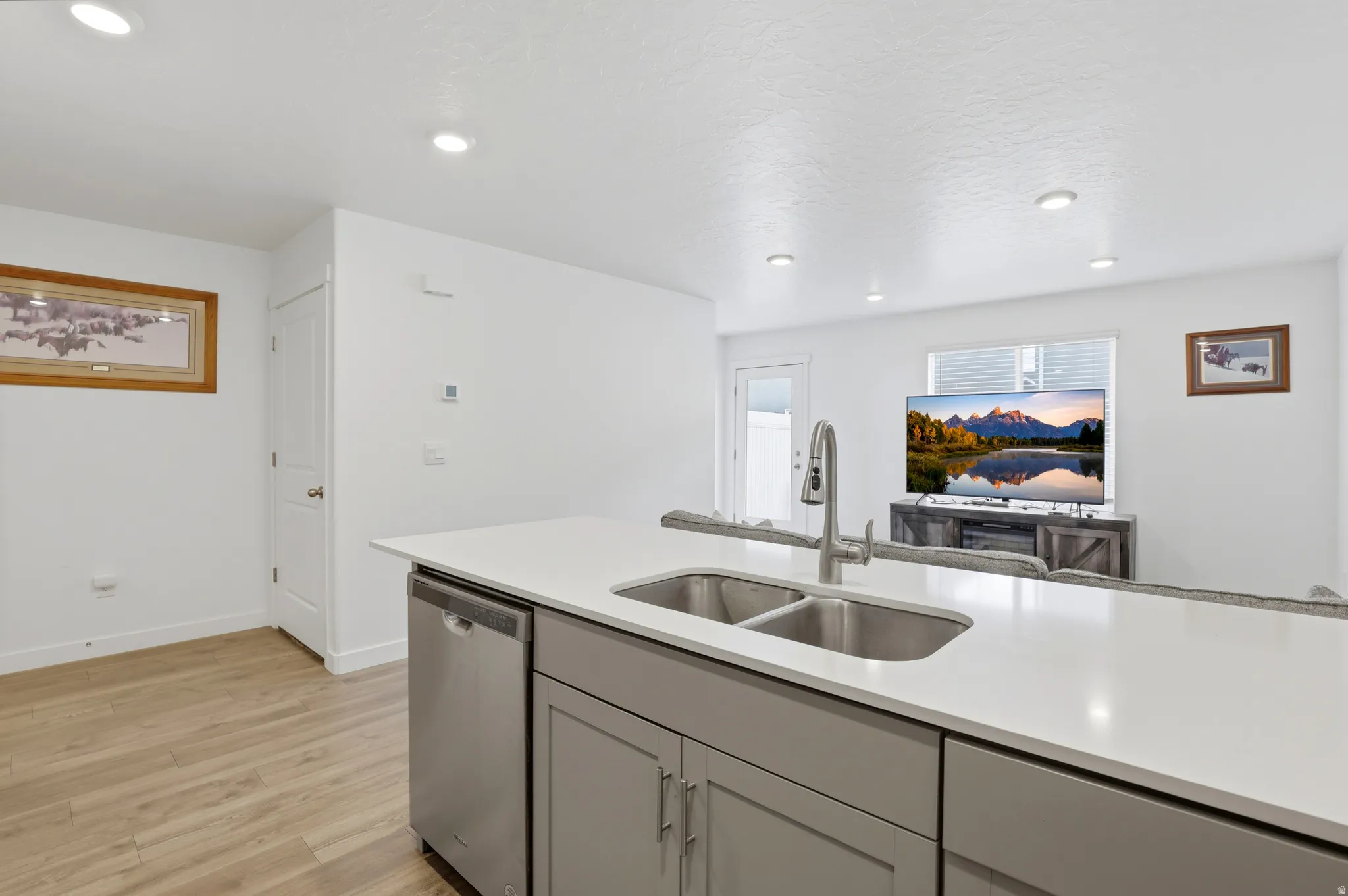 Kitchen island featuring a double basin stainless steel sink with a gooseneck faucet, light grey cabinetry, and white countertops