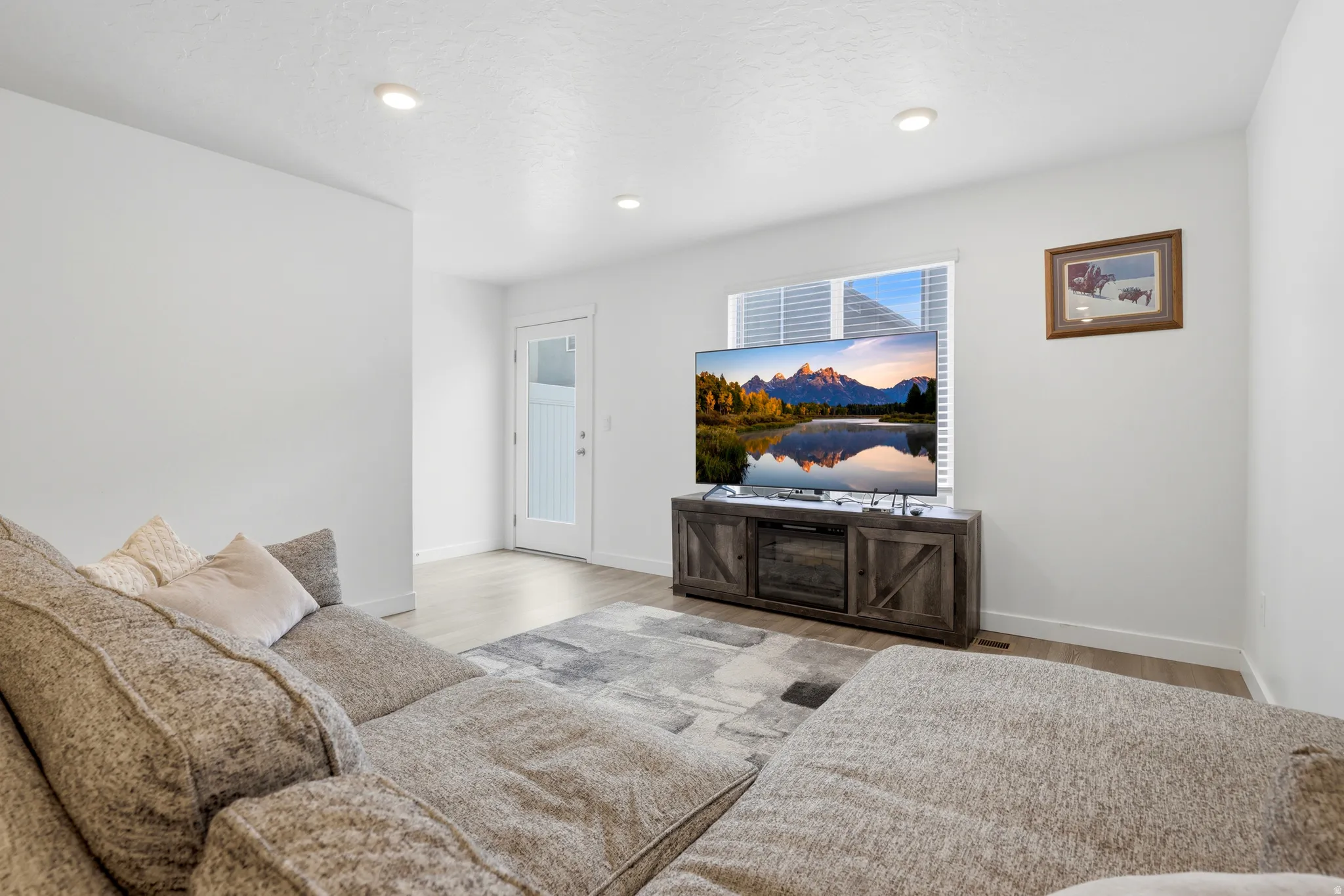 Living area featuring recessed lighting, a window with horizontal blinds, light wood-finish flooring, and a white paneled door