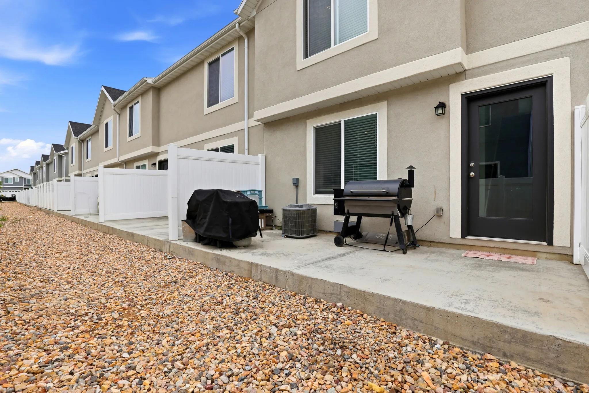 Rear patio with concrete surface, white privacy fencing, gravel landscaping, stucco exterior, and black framed windows