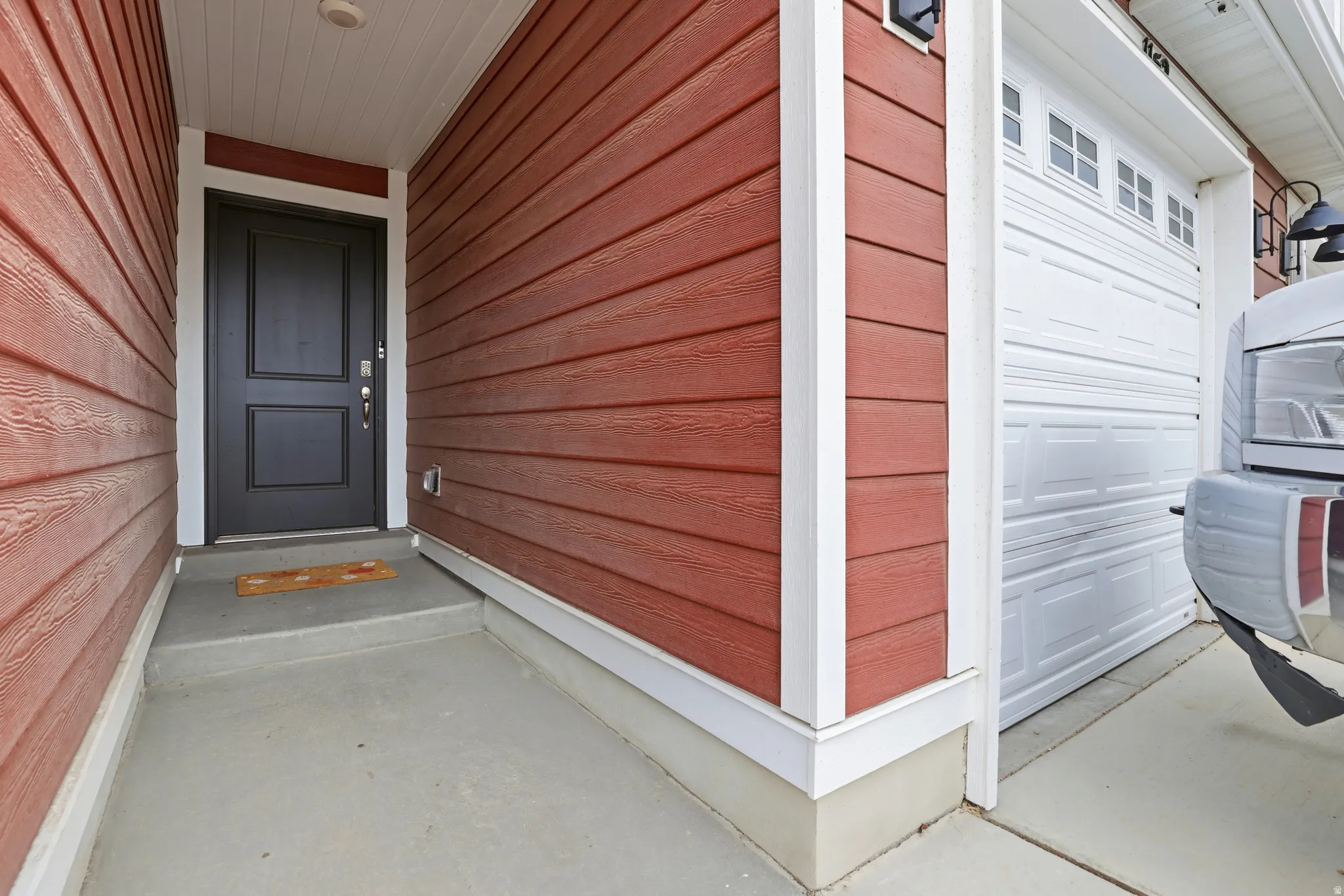 Entryway featuring a dark paneled door with white trim, red siding, and an overhead light fixture