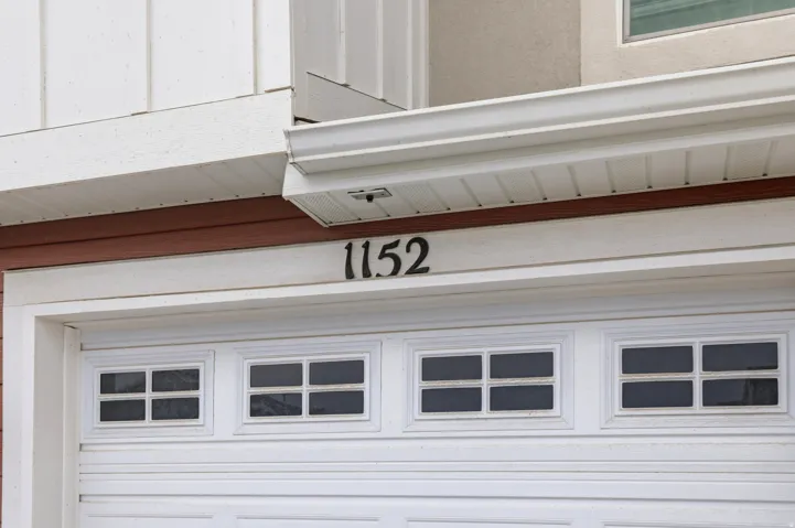 White paneled garage door with upper window inserts, featuring dark house numbers prominently displayed above the garage entrance