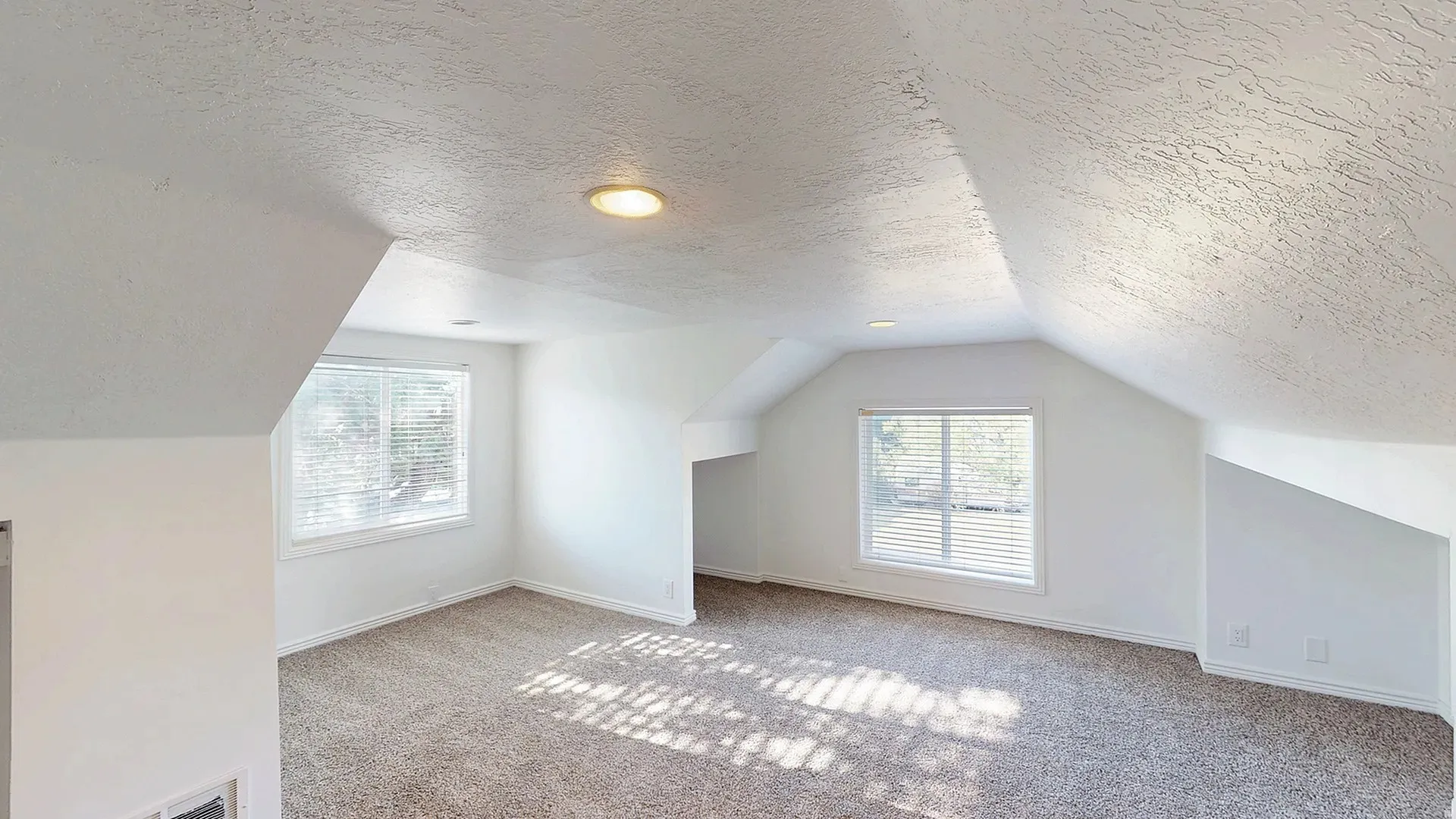 Spacious room featuring sloped ceilings, two windows with blinds, recessed lighting, and neutral-toned carpeting