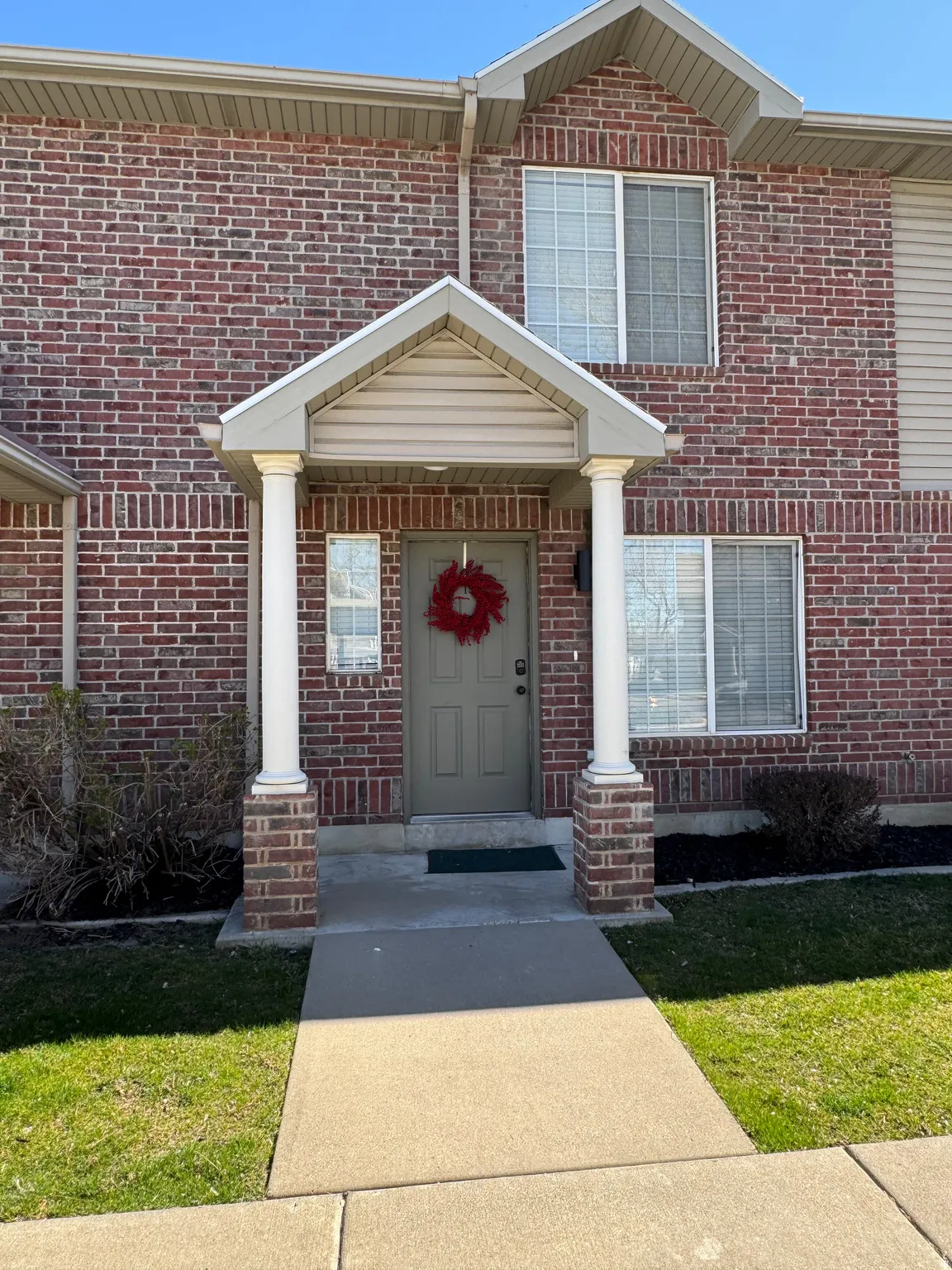 Brick exterior featuring an entryway portico with two columns and a paneled front door