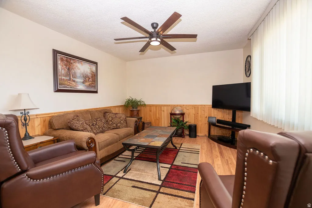 Living area featuring wood-finish flooring, wood paneling, and a ceiling fan with integrated lighting