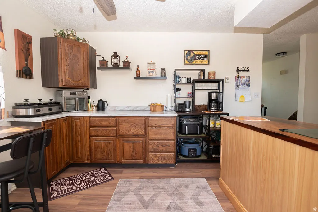 Kitchen featuring wood-finish flooring, wood cabinetry, light-toned countertops, and an integrated wood-paneled breakfast bar