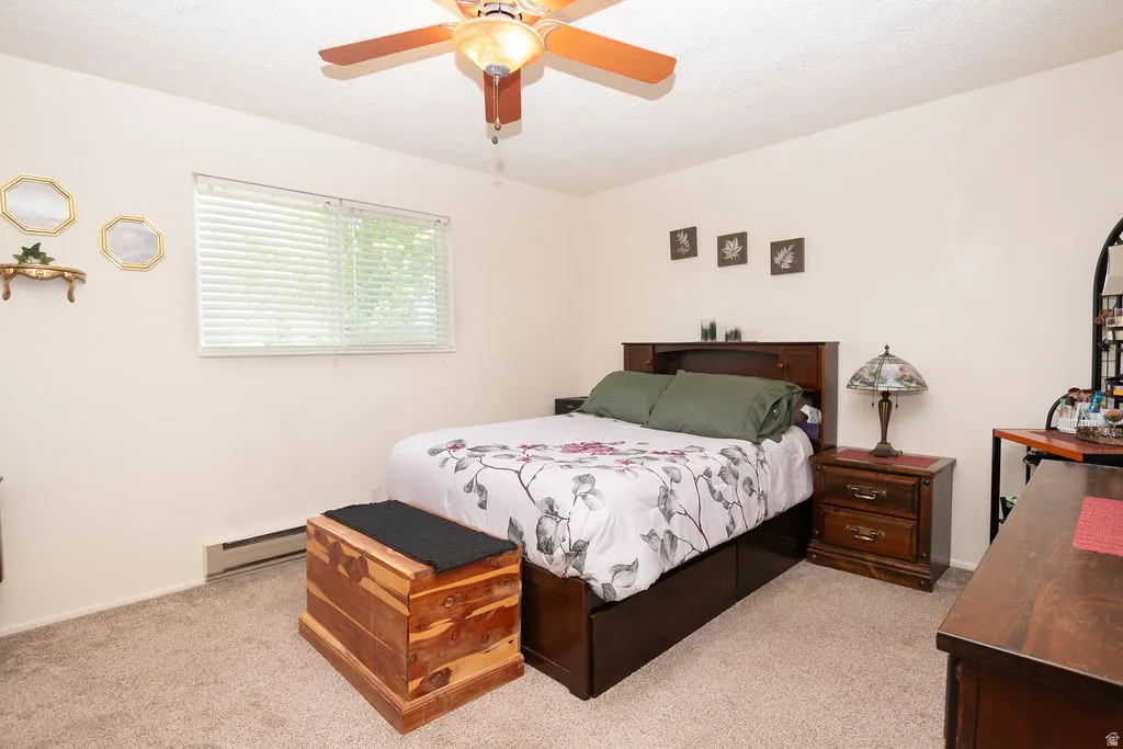 Carpeted room featuring a ceiling fan with integrated lighting, a window with horizontal blinds, and a baseboard heating unit