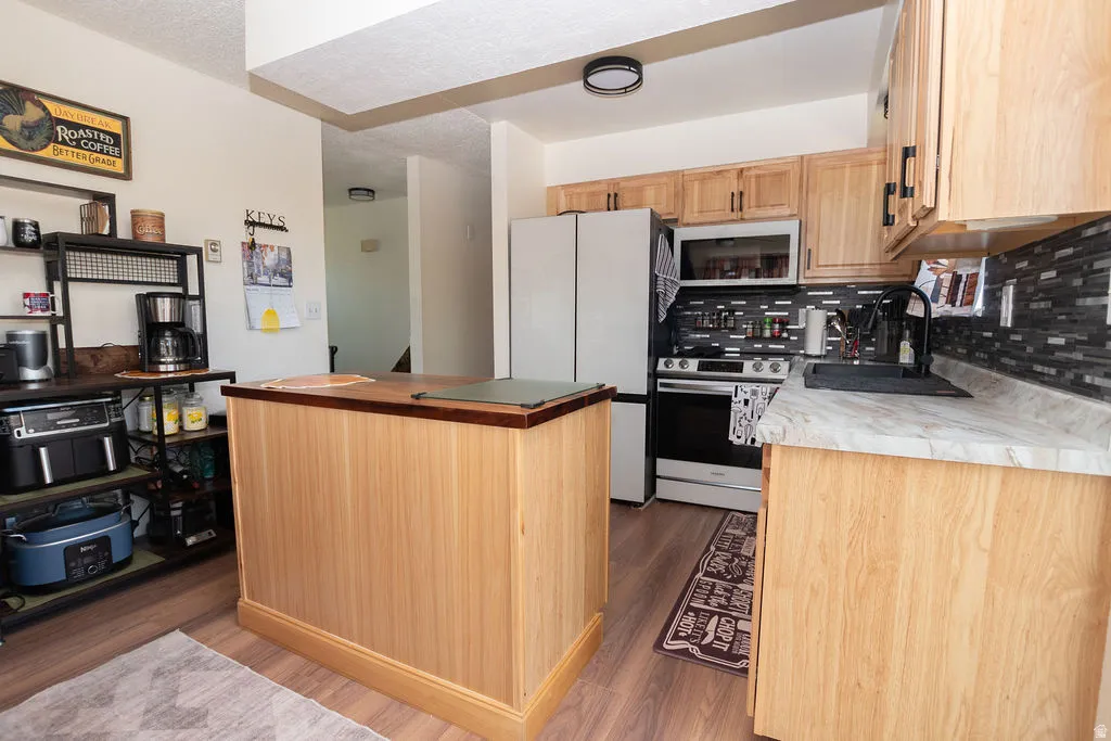 Kitchen featuring wood-finish flooring, wood cabinetry with dark hardware, a center island with a wood countertop, light-colored countertops, and a dark tile backsplash