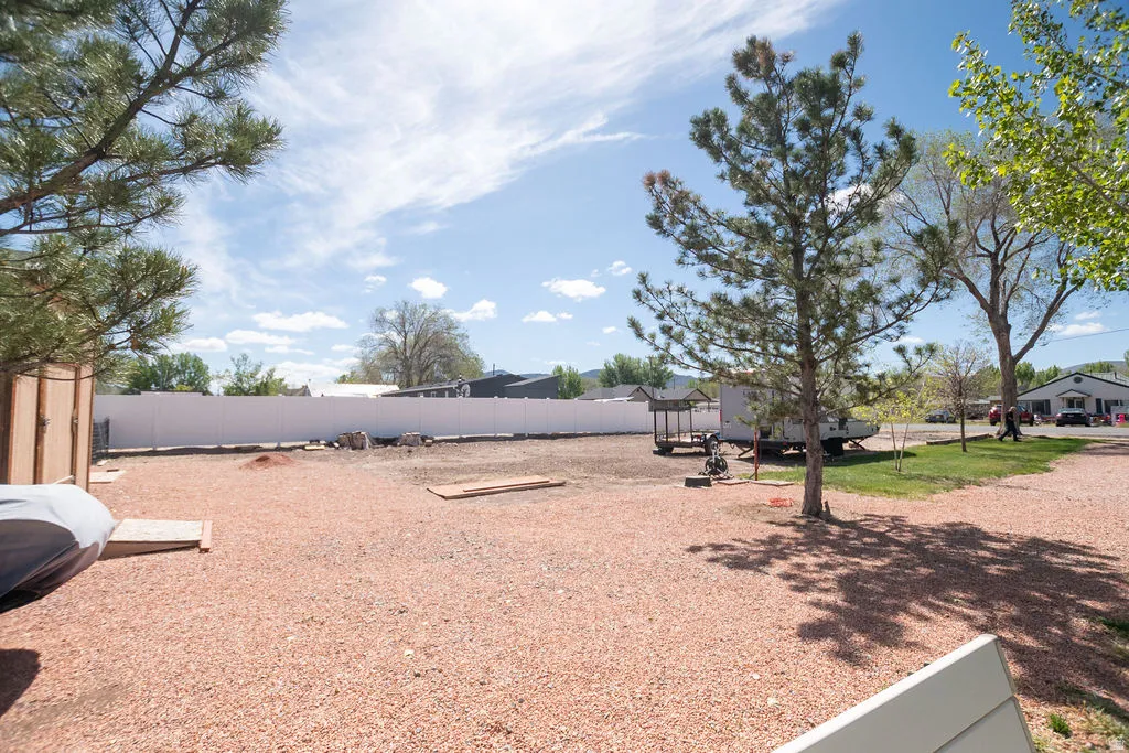 Expansive gravel lot with mature trees, a white perimeter fence, and partial grassy areas