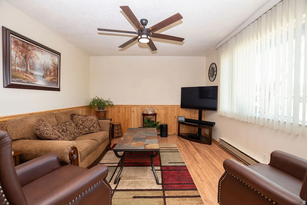 Living area with wood-finish flooring, wainscoting, and a ceiling fan with integrated lighting