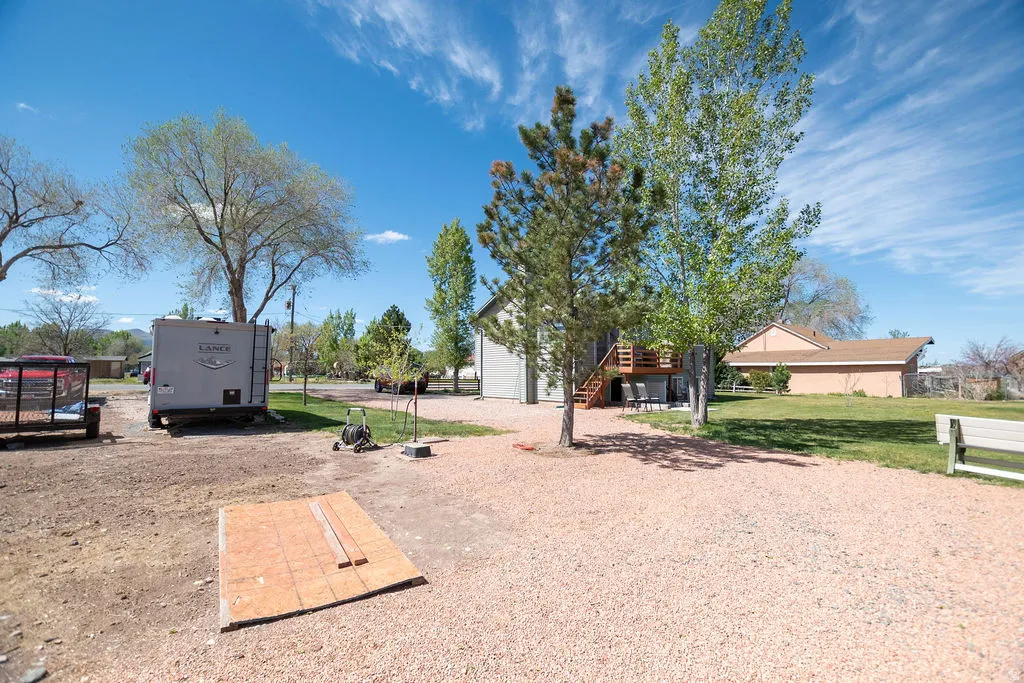 Spacious outdoor area featuring a gravel driveway, mature trees, and a grassy lawn