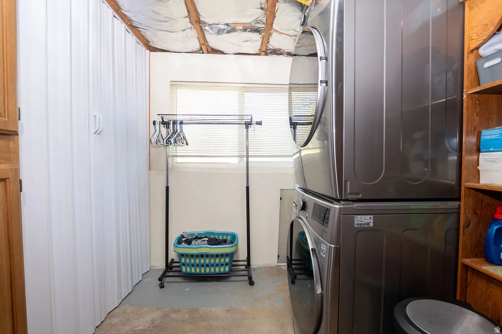 Laundry area featuring a stacked washer and dryer, a window with blinds, and built-in storage cabinetry