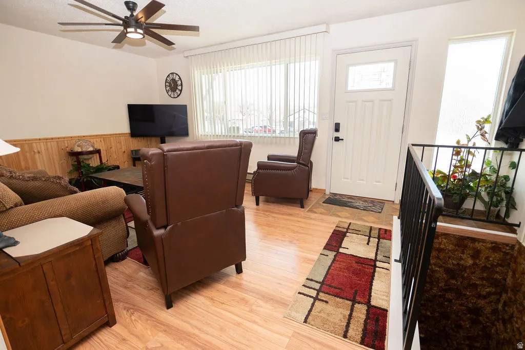 Living area featuring wood-finish flooring, a ceiling fan with integrated lighting, and wood paneling on the lower walls