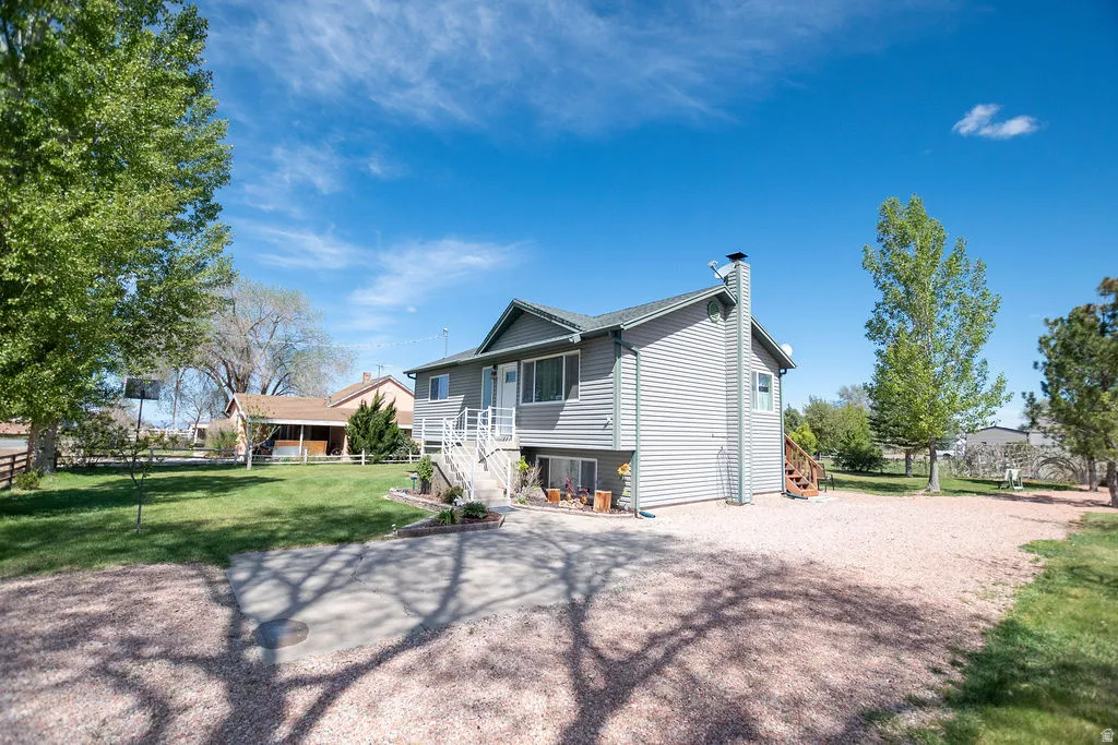 Split-level residence featuring gray siding, a white front porch with railings, a gravel driveway, and mature landscaping