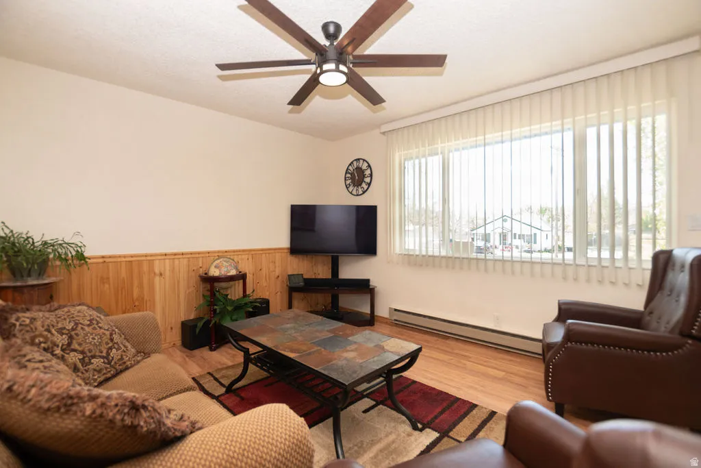Spacious living area featuring wood-finish flooring, a contemporary ceiling fan with integrated lighting, and a large window with vertical blinds