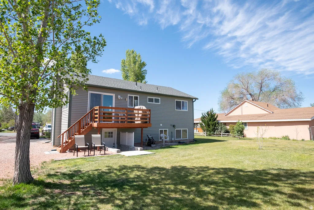 Rear exterior featuring a raised wood deck with staircase, sliding glass door access, ground-level patio, and horizontal siding