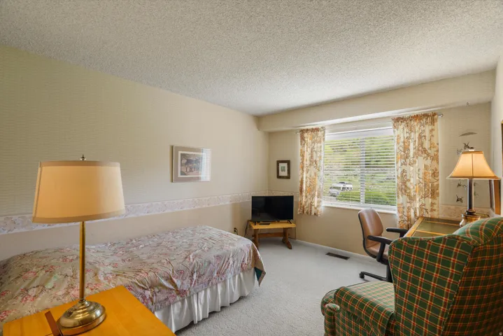 Carpeted room featuring a wide window with blinds, textured wallpaper, and a popcorn ceiling
