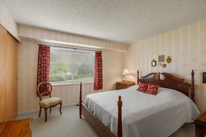 Room featuring a wide window with horizontal blinds, textured wall covering, light-colored carpeting, and a wood-finish bi-fold closet door