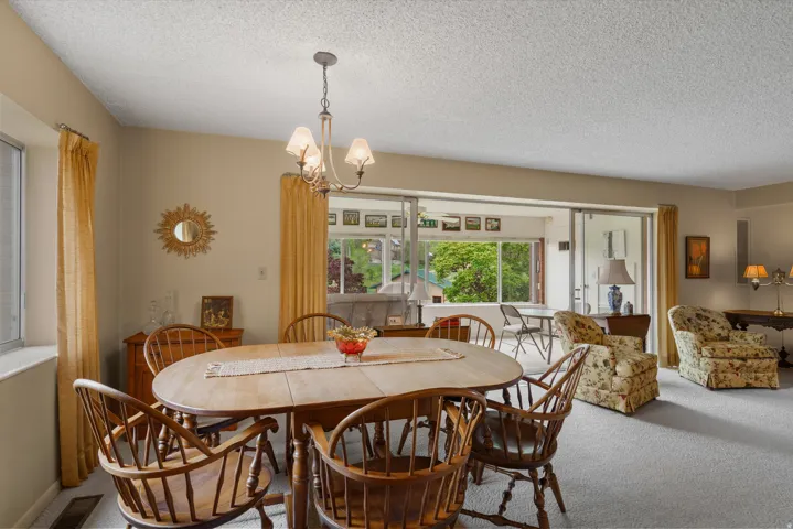 Dining area featuring a wood-finish oval table, coordinating wood-finish Windsor chairs, a brass chandelier, and light-colored carpet flooring