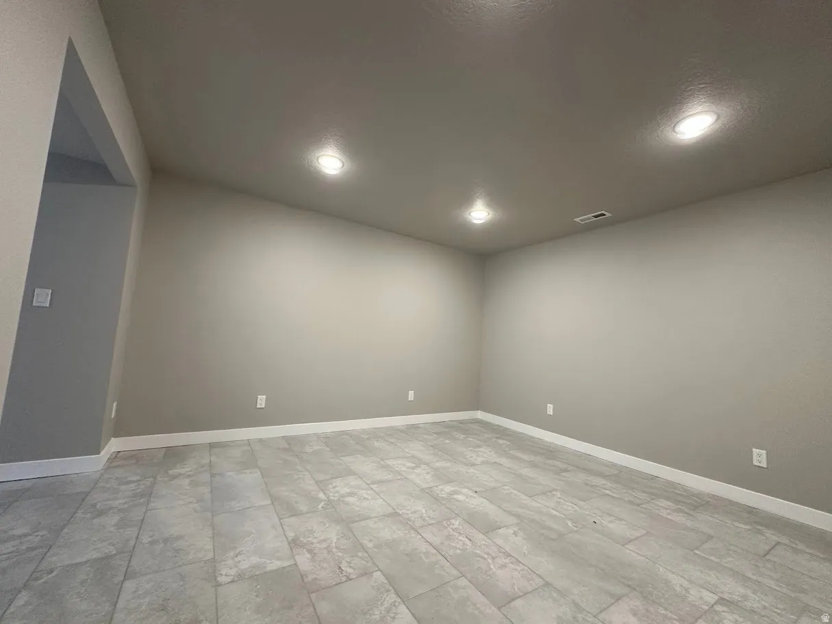 Spacious interior room featuring light gray walls, large format tile flooring, white baseboards, and recessed ceiling lighting
