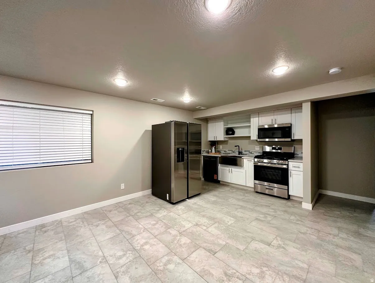 Contemporary kitchen featuring stainless steel appliances, white cabinetry, a tile backsplash, and light-toned tile flooring