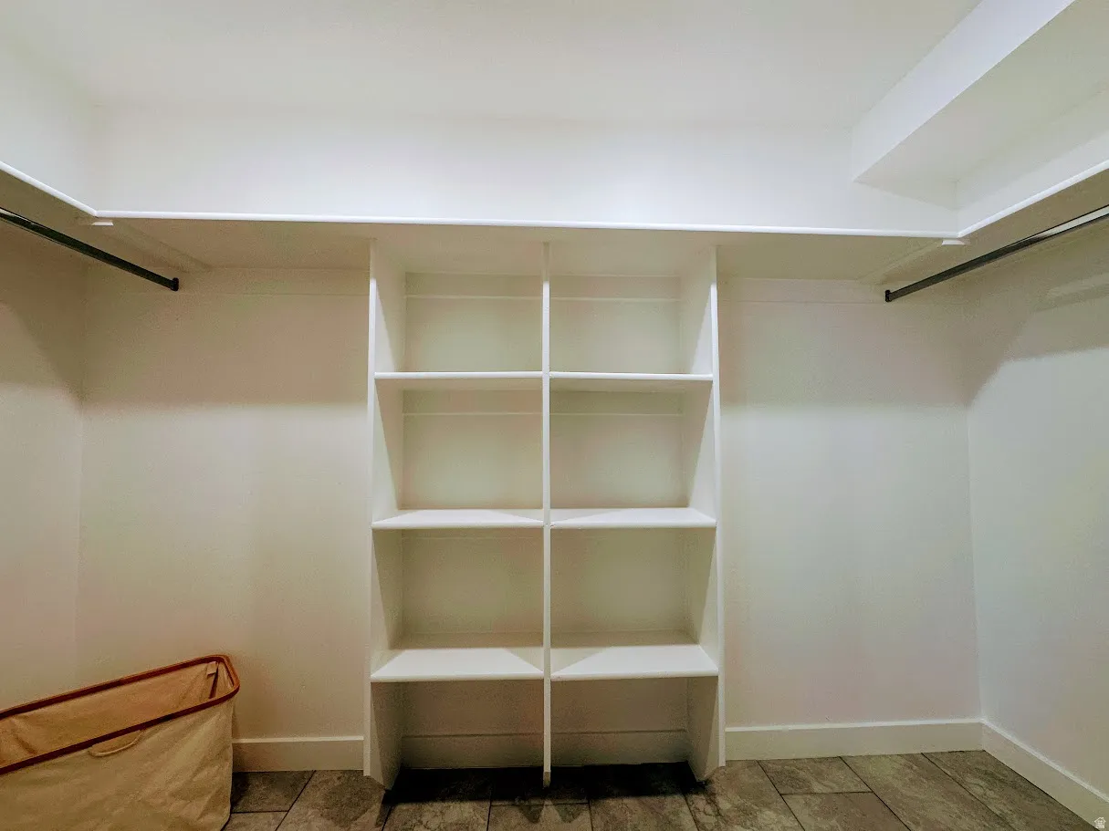 Walk-in closet featuring white built-in shelving, two hanging rods, white walls, and stone-finish flooring