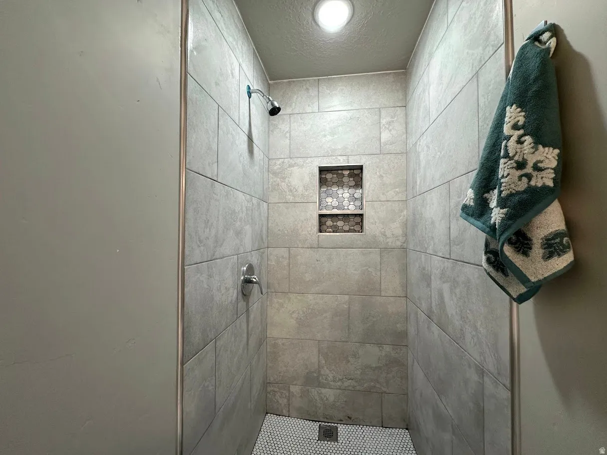 Shower stall with light grey rectangular tile walls and a white hex tile floor