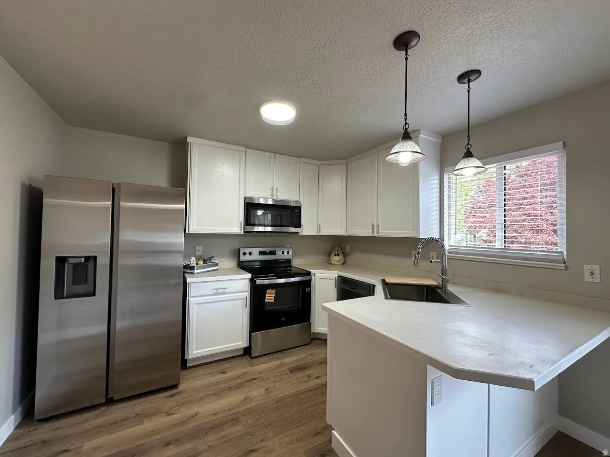 Kitchen featuring white shaker-style cabinetry, wood-finish flooring, stainless steel appliances, light-toned countertops, and a double basin sink with a gooseneck faucet