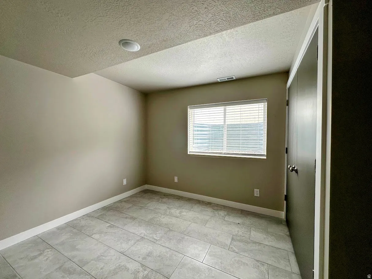 Spacious room featuring tile flooring, neutral wall paint, a window with blinds, recessed lighting, and a dark-paneled closet