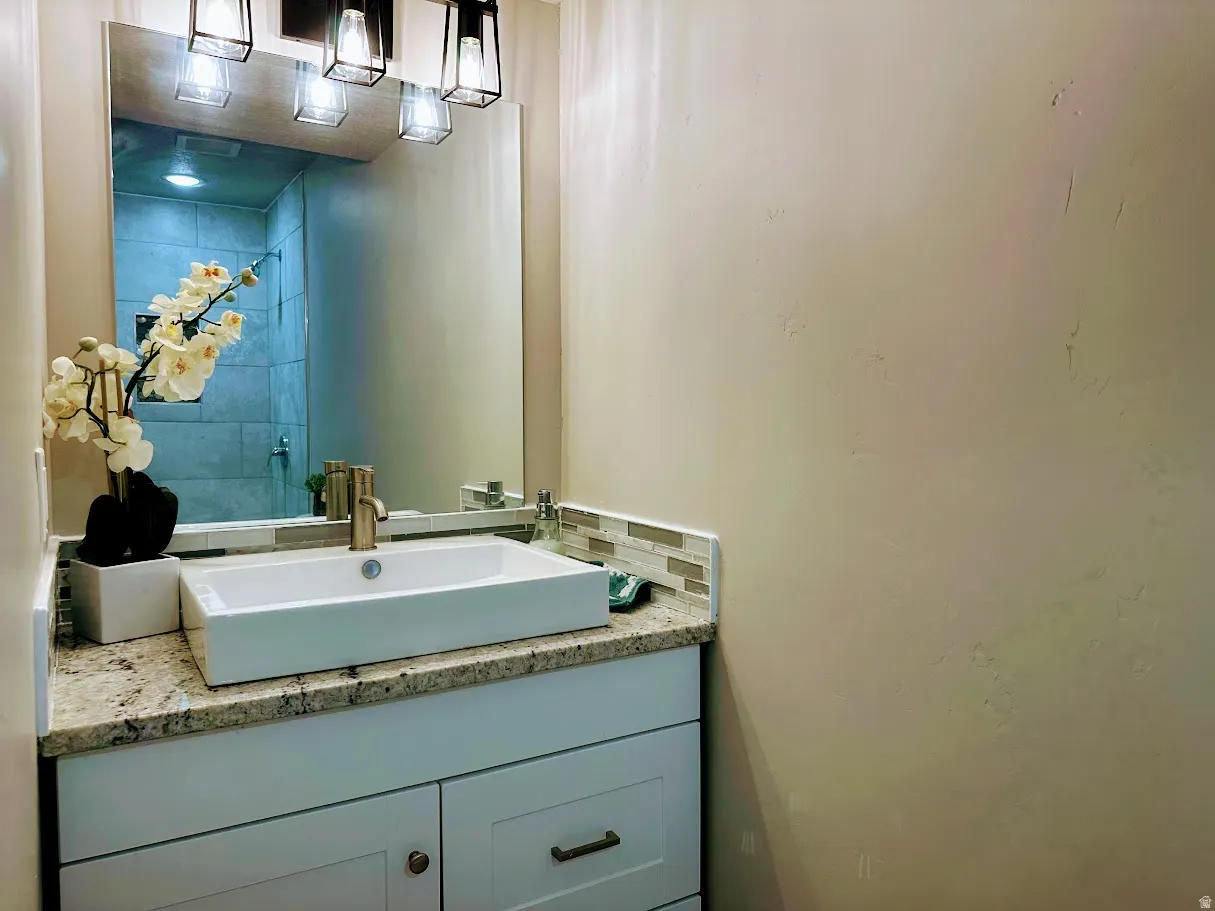 White rectangular vessel sink with a brushed brass faucet, set on a granite countertop with a mosaic tile backsplash