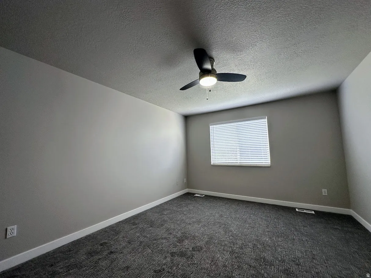 Spacious room featuring neutral painted walls, textured ceiling, and dark patterned carpet