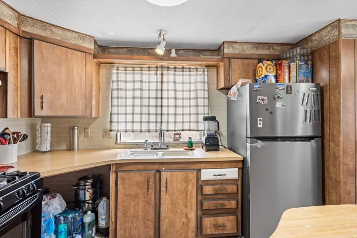 U-shaped kitchen featuring wood-finish cabinetry, light-toned countertops, and a stainless steel refrigerator