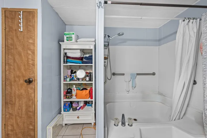 Built-in shower and tub combination featuring a shower head with hose, grab bar, and white shower curtain